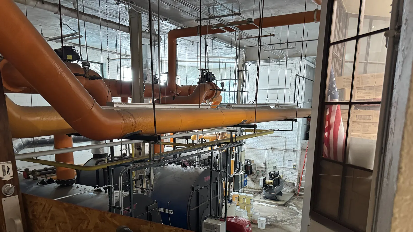 Boilers and insulated piping in a high school boiler room, the kind of commercial equipment an HVAC rebate application covers