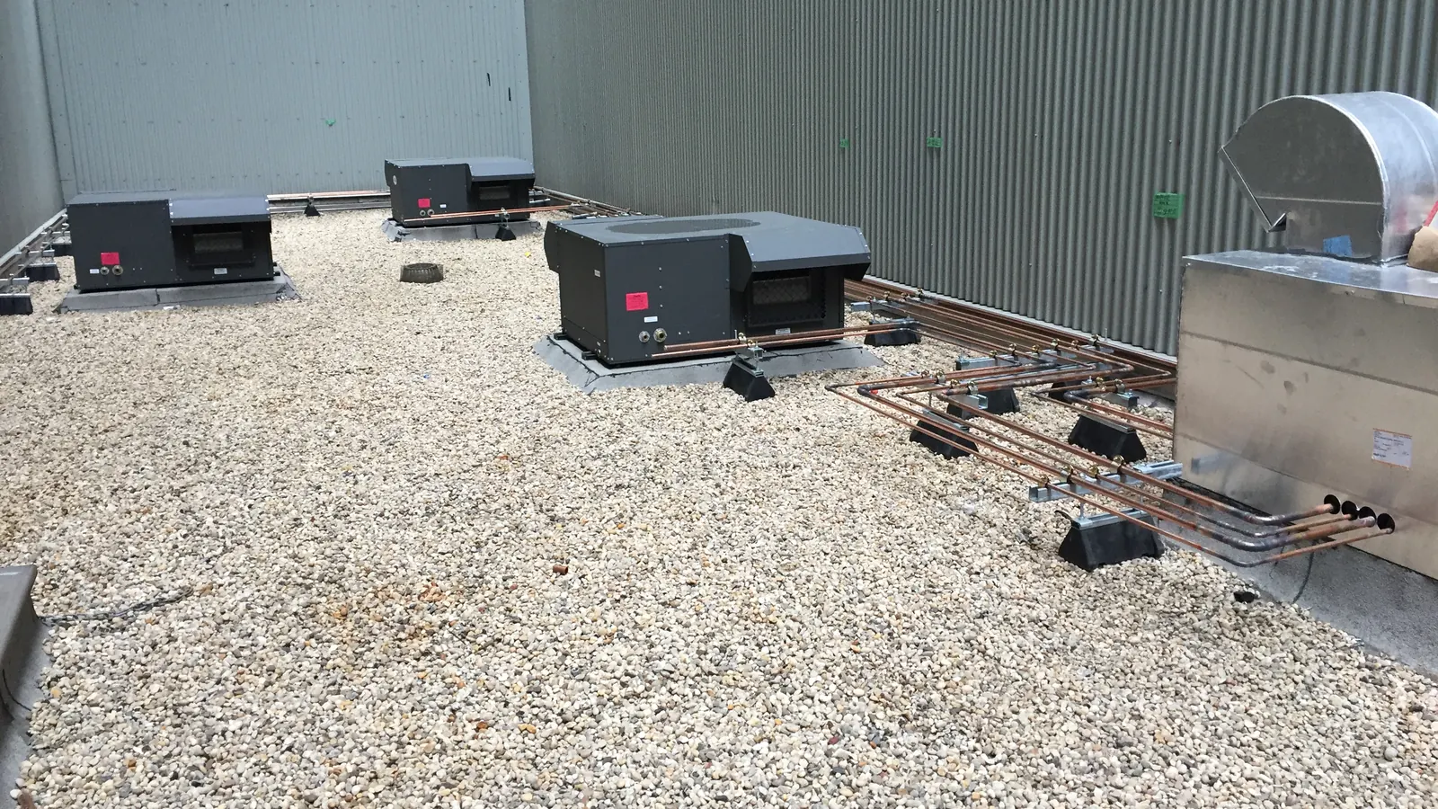 New rooftop HVAC units and copper refrigerant piping on a flat gravel roof, the kind of upgrade an HVAC replacement assistance program in NJ helps pay for